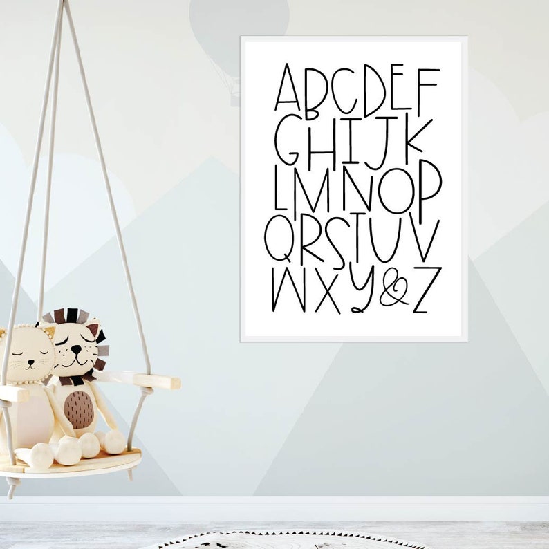 May include: A white framed print with black text that reads "ABCDEFGHIJKLMNOPQRSTUVWXYZ&" in a simple, modern font.