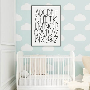 May include: A black framed print with white background and black text. The text reads "ABCDEFGHIJKLMNOPQRSTUVWXYZ". The print is hanging on a light blue wall with white cloud patterns.