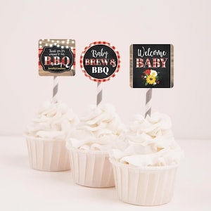Op de afbeelding: Drie cupcakes met witte frosting, bedekt met cupcake-toppers in rood-wit ruitjes, houtlook en schoolbord. De toppers zeggen "Bedankt voor het komen naar onze BBQ", "Baby Brew & BBQ" en "Welkom Baby".
