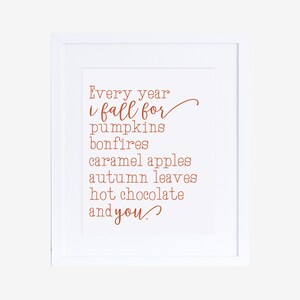 May include: A white framed print with a handwritten quote in orange text that reads "Every year i fall for pumpkins bonfires caramel apples autumn leaves hot chocolate and you."
