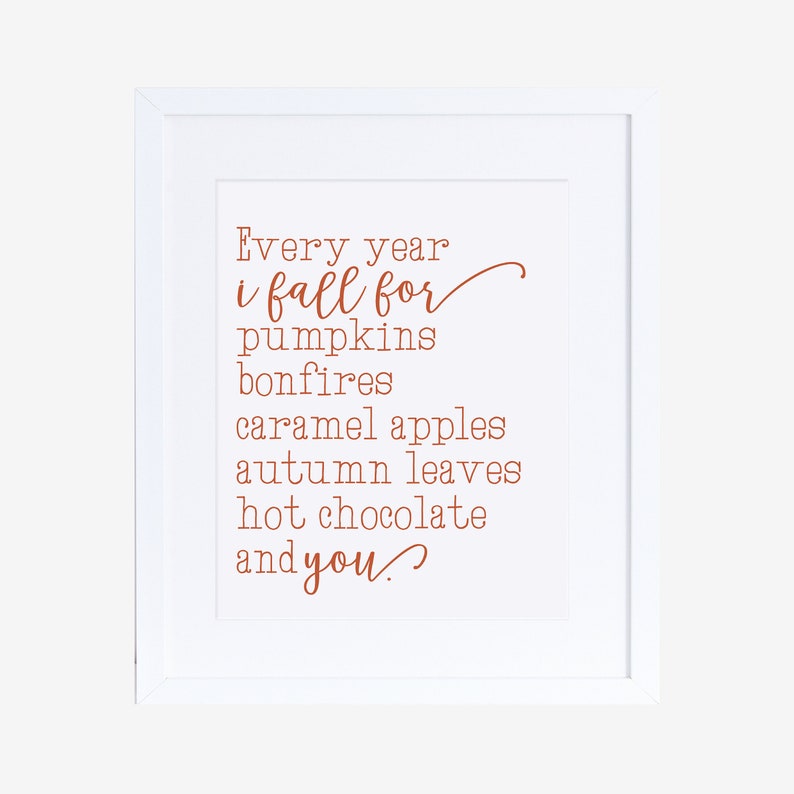 May include: A white framed print with a handwritten quote in orange text that reads "Every year i fall for pumpkins bonfires caramel apples autumn leaves hot chocolate and you."