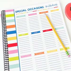 Pode incluir: Uma agenda branca com uma capa listrada colorida e uma encaderna&ccedil;&atilde;o em espiral preta. A agenda tem uma se&ccedil;&atilde;o para ocasi&otilde;es especiais e anivers&aacute;rios, com cada m&ecirc;s rotulado em uma faixa colorida. Os meses s&atilde;o janeiro, fevereiro, mar&ccedil;o, abril, maio, junho, julho, agosto, setembro, outubro, novembro e dezembro.