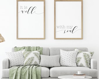 May include: Two framed prints with inspirational quotes. The left print says "it is well" in cursive script. The right print says "with my soul" in cursive script. The prints are hanging on a white wall above a gray couch with throw pillows.