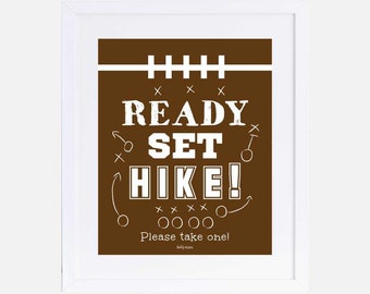 May include: A brown and white printable sign with the text "READY SET HIKE!" and football play diagrams. The sign says "Please take one!" at the bottom.