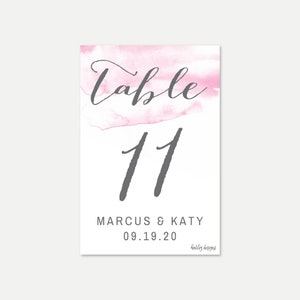 May include: Pink watercolor table number card with the number 11, the names Marcus & Katy, and the date 09.19.20. The text "Table" is written in cursive above the number. The text "holly designs" is written in a smaller font at the bottom of the card.
