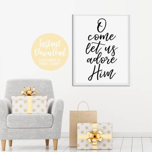 K&ouml;nnte beinhalten: Ein wei&szlig;er gerahmter Druck mit schwarzer Kalligraphie, auf dem "O come let us adore Him" steht. Der Druck h&auml;ngt an einer wei&szlig;en Wand mit einem grauen Sessel und verpackten Geschenken im Vordergrund.