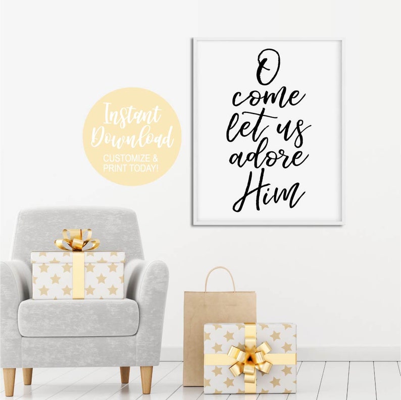 K&ouml;nnte beinhalten: Ein wei&szlig;er gerahmter Druck mit schwarzer Kalligraphie, auf dem "O come let us adore Him" steht. Der Druck h&auml;ngt an einer wei&szlig;en Wand mit einem grauen Sessel und verpackten Geschenken im Vordergrund.