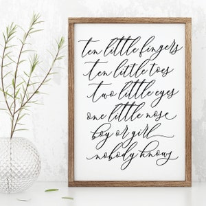 May include: A framed print with a white background and black calligraphy text that reads "ten little fingers, ten little toes, two little eyes, one little nose, boy or girl, nobody knows".