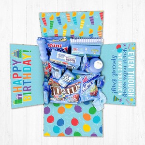 May include: A blue and white gift box filled with various blue and colorful snacks and treats. The box has a happy birthday message on the front and a message that says "Even though you're miles away, we hope you have a special day!" on the side.