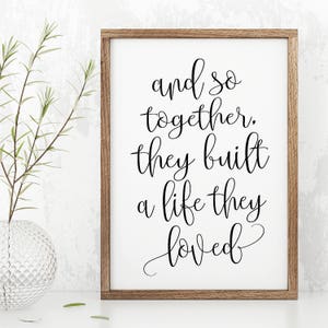 May include: A framed print with a white background and black calligraphy text that reads "and so together, they built a life they loved".