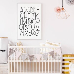 May include: A white crib with a pink and gray bunting hanging above it. The crib is decorated with pillows and a white frame with black letters spelling out the alphabet. The letters are in a simple, modern font.