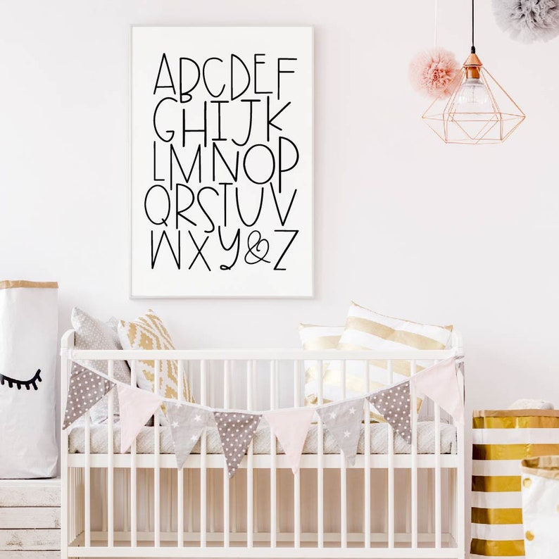 May include: A white crib with a pink and gray bunting hanging above it. The crib is decorated with pillows and a white frame with black letters spelling out the alphabet. The letters are in a simple, modern font.