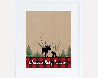 Puede incluir: Una tarjeta marrón con un borde de cuadros rojos y negros. La tarjeta presenta una silueta de un alce y un alce bebé en un entorno de bosque. El texto "Welcome Baby Swanson" está impreso en la tarjeta.