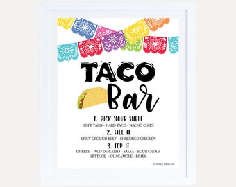 May include: A white sign with the text "TACO Bar" in black lettering. The sign has a colorful paper garland at the top and a cartoon taco image. The sign lists the ingredients for a taco bar: "Pick your shell", "Fill it", and "Top it".