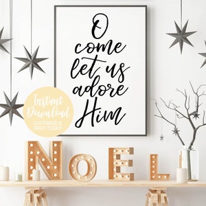 K&ouml;nnte beinhalten: Ein wei&szlig;er gerahmter Druck mit schwarzer Kalligraphie, auf dem "O come let us adore Him" steht. Der Druck h&auml;ngt an einer wei&szlig;en Wand mit einem Holzregal darunter. Das Regal hat einen Satz Holzbuchstaben, die "NOEL" buchstabieren, mit Gl&uuml;hbirnen in jedem Buchstaben.