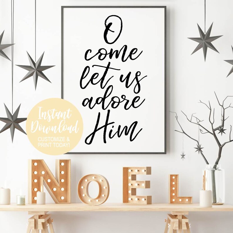 K&ouml;nnte beinhalten: Ein wei&szlig;er gerahmter Druck mit schwarzer Kalligraphie, auf dem "O come let us adore Him" steht. Der Druck h&auml;ngt an einer wei&szlig;en Wand mit einem Holzregal darunter. Das Regal hat einen Satz Holzbuchstaben, die "NOEL" buchstabieren, mit Gl&uuml;hbirnen in jedem Buchstaben.