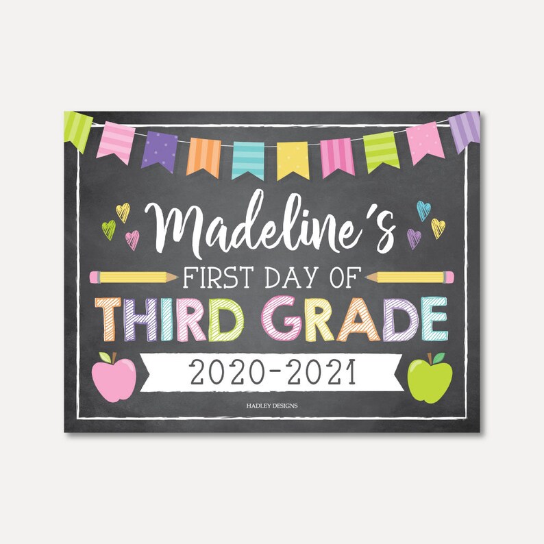 May include: A chalkboard sign with a colorful banner at the top, reading "Madeline's First Day of Third Grade 2020-2021". The sign is decorated with hearts, pencils, and apples.