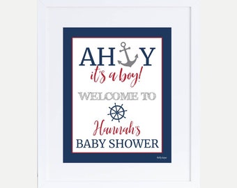 Könnte beinhalten: Ein weiß gerahmtes Schild mit blauem Hintergrund und weißem Text, der "Ahoy, es ist ein Junge! Willkommen zur Babyparty von Hannah" lautet. Das Schild zeigt außerdem einen grauen Anker und ein graues Steuerrad.