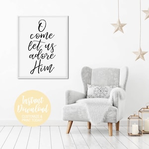 K&ouml;nnte beinhalten: Ein wei&szlig;er gerahmter Druck mit schwarzer Kalligraphie, auf dem "O come let us adore Him" steht. Der Druck h&auml;ngt an einer wei&szlig;en Wand &uuml;ber einem grauen Sessel mit einer wei&szlig;en Wolldecke und einem Kissen mit Schneeflockenmuster. An der Decke h&auml;ngen zwei goldene Sterne.
