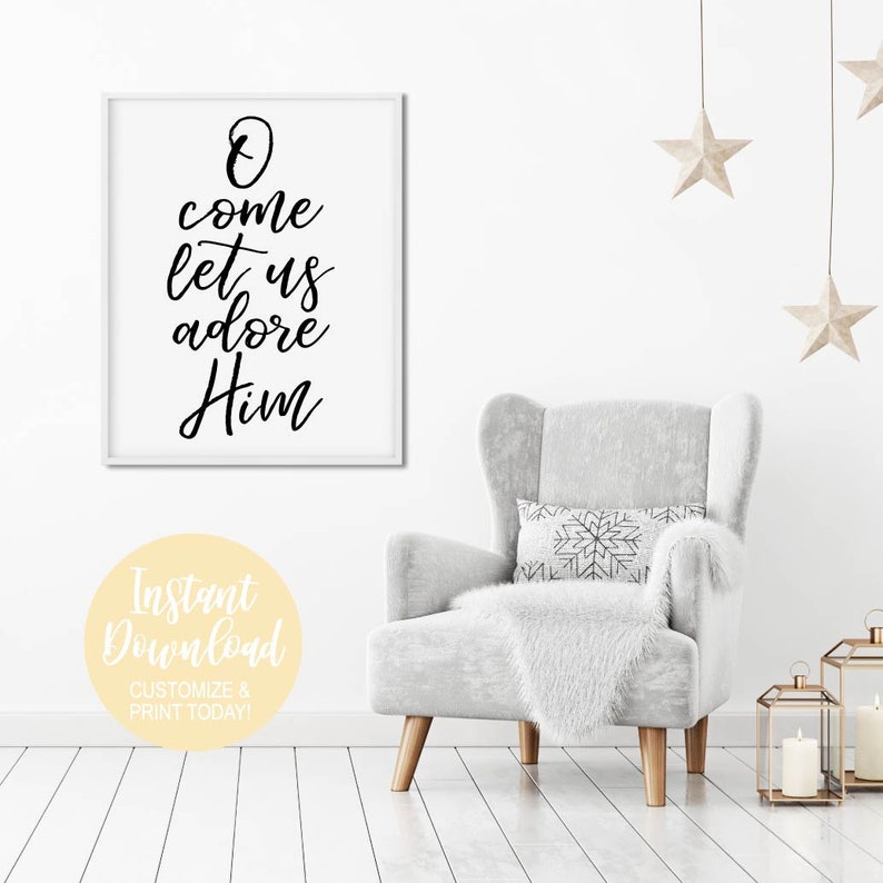 K&ouml;nnte beinhalten: Ein wei&szlig;er gerahmter Druck mit schwarzer Kalligraphie, auf dem "O come let us adore Him" steht. Der Druck h&auml;ngt an einer wei&szlig;en Wand &uuml;ber einem grauen Sessel mit einer wei&szlig;en Wolldecke und einem Kissen mit Schneeflockenmuster. An der Decke h&auml;ngen zwei goldene Sterne.