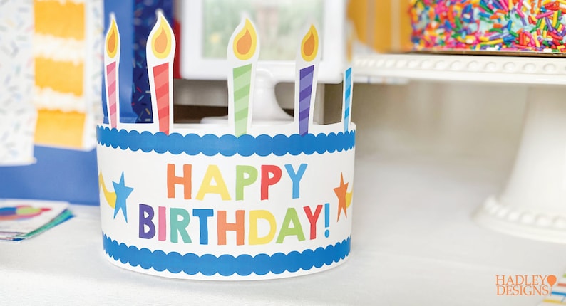 Puede incluir: Un gorro de cumplea&ntilde;os de papel colorido con forma de pastel con velas y las palabras "&iexcl;Feliz cumplea&ntilde;os!" en la parte delantera.