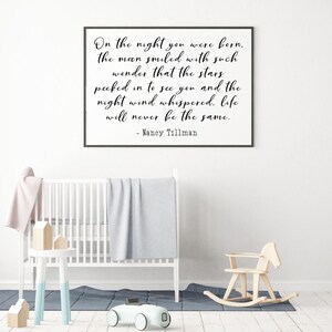 Op de afbeelding: Een zwart ingelijst print met een witte achtergrond en een citaat in zwarte schrijfletters dat luidt: "On the night you were born, the moon smiled with such wonder that the stars peeked in to see you and the night wind whispered, life will never be the same. - Nancy Tillman"