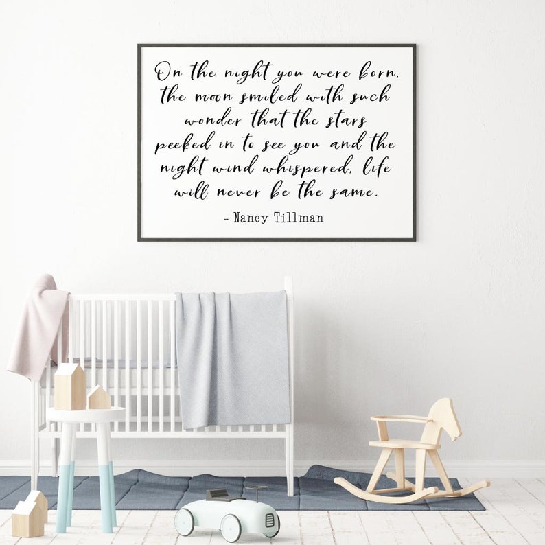Op de afbeelding: Een zwart ingelijst print met een witte achtergrond en een citaat in zwarte schrijfletters dat luidt: "On the night you were born, the moon smiled with such wonder that the stars peeked in to see you and the night wind whispered, life will never be the same. - Nancy Tillman"