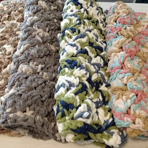 May include: Four crocheted blankets in different color combinations. The blankets are made with a chunky yarn and have a textured, fluffy look. The colors include beige, gray, green, blue, and pink.