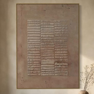 May include: A large, framed abstract artwork with a textured, rectangular design in beige and brown tones. The artwork hangs above a wooden bench in a neutral-toned room. A vase with branches sits on the bench.