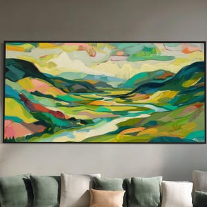 May include: A large, rectangular abstract landscape painting in a black frame. The artwork uses a vibrant mix of colours, including green, yellow, and blue, depicting rolling hills and a river. The painting hangs above a white sectional sofa with green and tan cushions.