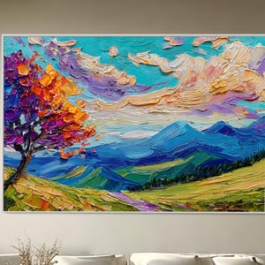Op de afbeelding: Een levendig landschapsschilderij met een boom met paarse en oranje bladeren, groene heuvels en blauwe bergen onder een lucht met pluizige wolken. Het kunstwerk is ingelijst en wordt tentoongesteld in een moderne woonkamer.