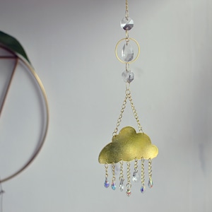 May include: A gold metal cloud-shaped ornament with a chain hanging from it. The cloud has a gold finish and is decorated with clear crystal raindrops.