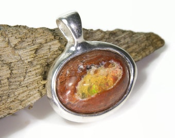 May include: A silver pendant with a red and brown opal gemstone. The opal has a green and yellow iridescent sheen.