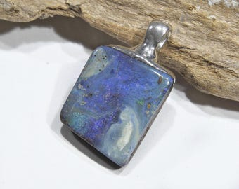 May include: A rectangular pendant with a vibrant blue and purple opal stone. The stone has a unique pattern with hints of green and white. The pendant is set in a silver metal frame with a loop for a chain.