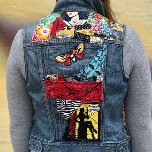 May include: A blue denim vest with a variety of colorful fabric patches sewn on the back. The patches include a butterfly, a woman's face, and a comic book panel with the text "Oh yes Jill I'm coming tomorrow at noon!"