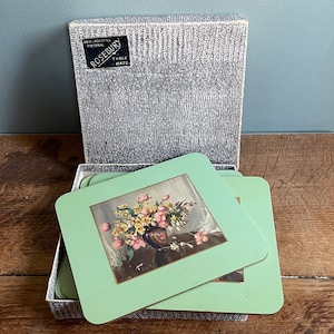 May include: A set of six green floral coasters in a box. The coasters feature a floral design with a vase of pink and yellow flowers. The box is labelled "Rosebury Table Mats."
