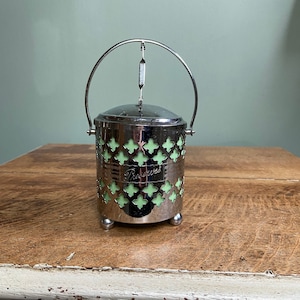 May include: Silver and green glass jar with a decorative metal lid and a handle. The jar has a cutout design and the words "Preserves" written on the front.