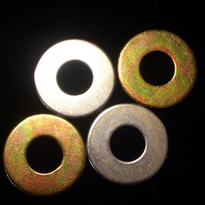 May include: Four metal washers with a central hole are displayed against a black background. Two washers have a silver finish, while the other two have a gold-colored finish. The washers are circular and appear to be made of steel.