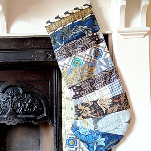 May include: A patchwork Christmas stocking, featuring a mix of patterned fabrics in blue, brown, and cream. The stocking hangs from a silver loop. The design incorporates floral, geometric, and abstract patterns, offering a unique festive decoration for the home.