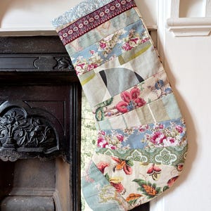May include: A patchwork Christmas stocking, featuring a mix of floral and patterned fabrics in blue, pink, and green hues. The stocking is suspended near a fireplace, displaying a festive, handcrafted design.