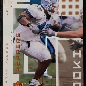 May include: A 2002 Rookie MVP football trading card featuring Julius Peppers in a light blue and white uniform. The card has the text "2002 Rookie" and "Peppers" in gold lettering. The background is a mix of blue and brown.