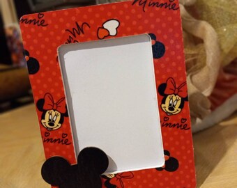 May include: Red picture frame with white polka dots and Minnie Mouse images. The frame has a black Mickey Mouse ear cutout on the bottom right corner. The text "Minnie" is written on the top right corner of the frame.