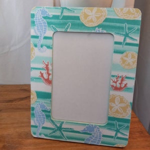 May include: A white picture frame with a green, blue, and yellow striped background. The frame features seahorse, starfish, and seashell designs.