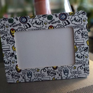 May include: White picture frame with a black and yellow comic book design featuring the Avengers characters. The frame has a white background with black outlines and yellow accents. The text on the frame includes "Avengers", "Hulk", "Leader", "Team", and "Always Angry".