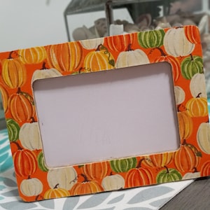 May include: A wooden picture frame with a white background and a border decorated with a pattern of orange, white, and green pumpkins.