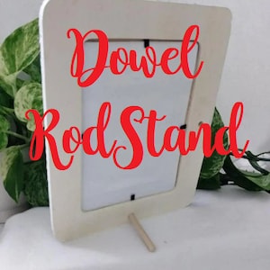 May include: White wooden picture frame with a dowel rod stand. The frame has a white mat and the text "Dowel Rod Stand" is written in red cursive.