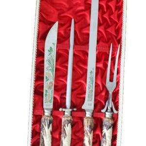 May include: A four-piece carving set featuring stainless steel blades and handles with textured brown and cream detailing. The set includes two knives, a sharpening steel, and a two-pronged fork, all presented in a rectangular case lined with red fabric.