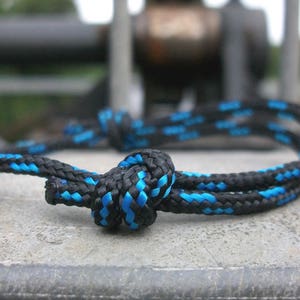 Könnte beinhalten: Ein schwarzes und blaues Seil, das zu einem Knoten gebunden ist. Das Seil ist mit blauen Akzenten geflochten.