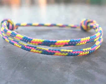 Peut inclure: Un bracelet tressé coloré avec des fils roses, jaunes, bleus et violets. Le bracelet est noué à chaque extrémité.