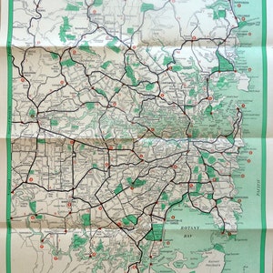 Puede incluir: Un mapa vintage de Sydney y sus suburbios, impreso en blanco y negro con acentos rojos y verdes. El mapa muestra las carreteras principales, los parques y los puntos de referencia. El mapa se titula "Map of Sydney and Suburbs" e incluye el texto "Copyright Clive Barrass Manly, N.S.W."